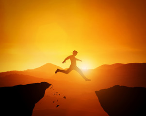 Man jumping from one rock to another. Sunset mountains scenery