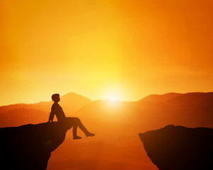 Man sitting relaxed on the edge of mountain looking at scenic sunset skyline.