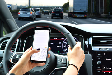 Naklejka premium Woman sending message from a smartphone while driving a car