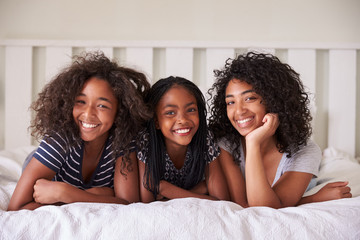 Portrait Of Three Teenage Sisters Lying On Bed At Home