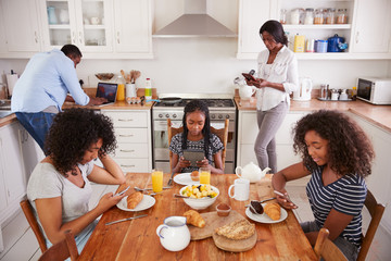 Family Sitting Around Breakfast Table Using Digital Devices