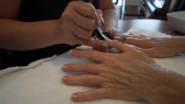 Tight shot of manicurist painting on salmon colored polish onto the fingernails of a caucasian woman.