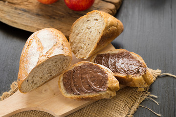 French bread baguette cut on wooden board with knife. with a chocolate butter and red apple.