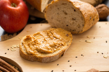 French bread baguette cut on wooden board with knife. with a peanut Butter and red apple.