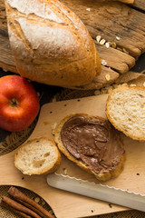 French bread baguette cut on wooden board with knife. with a chocolate butter and red apple.