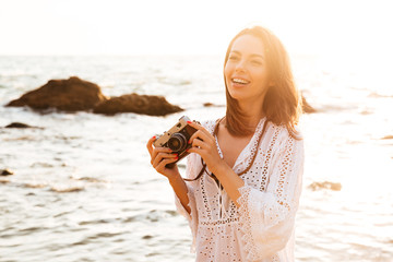 Fototapeta na wymiar Laughing brunette woman in light summer dress posing on beach