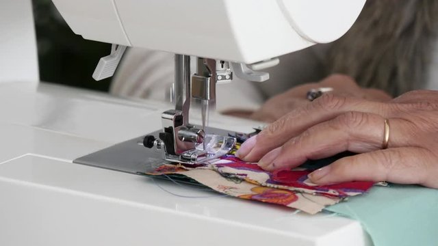 tailor sews on the sewing machine multi colored patchwork fabric