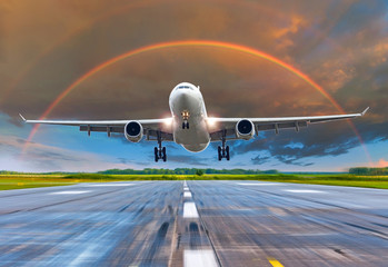 Passenger airplane landing at sunset rainbow on a runway