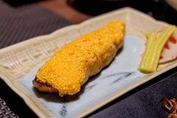Dish of Japanese grilled salmon fillet with mentaiko (shrimp or cod roe) white sauce in closeup view in restaurant