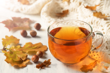 Cup of tea with autumn leaves and a knitted blanket on a wooden table.