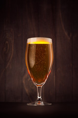 Goblet beer glass with golden sparkling lager on dark wood board, vertical. Template for advertising, design, branding identity, restaurant menu, cover.
