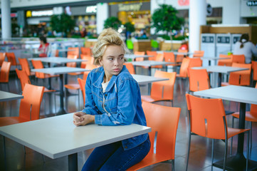 young beautiful woman in jeans clothes in business space of shopping center. portrait of a girl with freckles on her face, stylish girl in an empty cafe