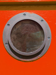 close up of rusty metal vintage porthole on a red wooden boat with screws in summer light