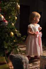 Cute toddler girl standing near Christmas tree