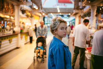 young beautiful woman in jeans clothes in business space of shopping center. portrait of a girl with freckles on her face, stylish girl standing near show-windows of fair in shopping center