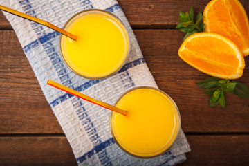 Orange juice in a glass on a wooden background with orange and melissa.
