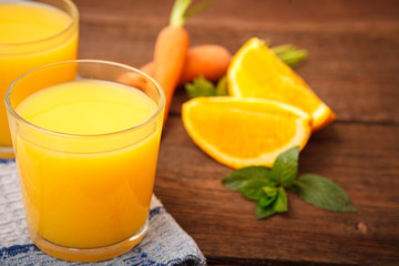 Refreshing orange-carrot juice in a glass on a wooden background. Carrots, orange, mint, Melissa and fruit and vegetable juice. Vitamins. Proper nutrition.