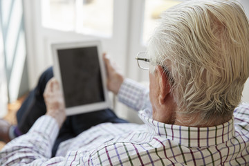 Senior man using tablet computer at home, over shoulder view