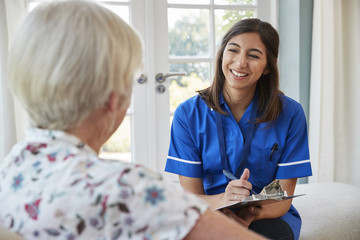 Senior woman sitting at home with care nurse taking notes