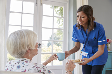 Fototapeta premium Nurse serving tea to senior woman at home, close up