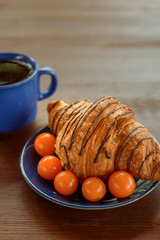 Morning breakfast: blue cup of tea, chocolate croissant and physalis on a wooden table
