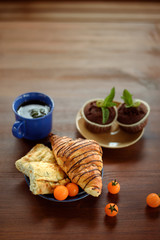 Morning breakfast: blue cup of tea, chocolate croissant, muffins and physalis on a wooden table
