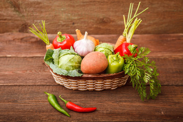 Fresh vegetables in a basket on a wooden background. Cabbage, bell pepper, potatoes, garlic, onion, chili and carrots. Harvest. Thanksgiving Day. Space for text.