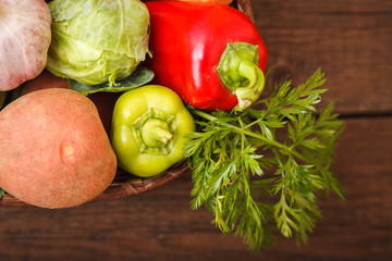 Fresh vegetables in a basket on a wooden background. Cabbage, bell pepper, potatoes, garlic, onion, chili and carrots. Harvest. Thanksgiving Day. Space for text.