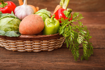 Fresh vegetables in a basket on a wooden background. Cabbage, bell pepper, potatoes, garlic, onion, chili and carrots. Harvest. Thanksgiving Day. Space for text.