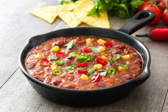 Traditional mexican tex mex chili con carne in a frying pan on wooden table
