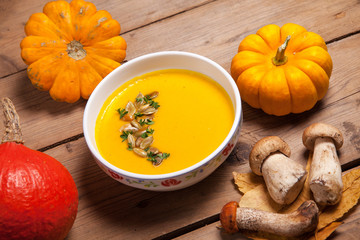 autumn still life, pumpkin soup with various pumpkins and forest mushrooms on a wooden table