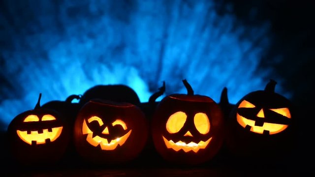 Halloween pumpkins in a row with candles over blue light rays and smoke at background with copy space for text above, front view, sliding video
