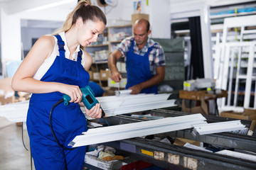 Young workwoman using electric drill on window frame