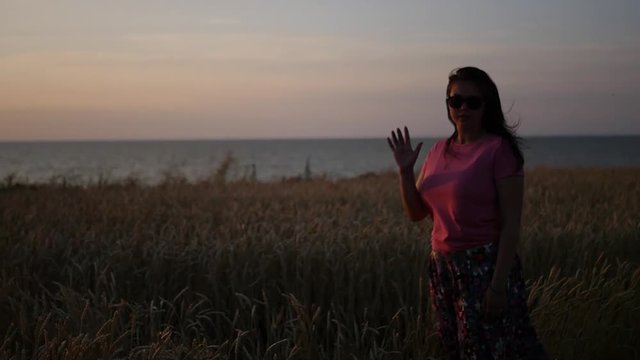 A girl stands in a field of wheat near the sea, waving her hand. HD, 1920x1080. slow motion.