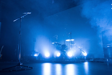 A kit of drums and a microphone on an empty stage in blue smoke before the concert