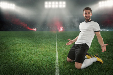 Siegreicher Fußballer bei Kniefall im Fußballstadion mit Flutlicht und Feuerwerk
