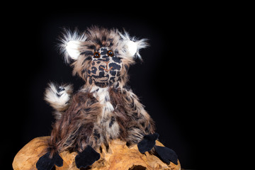 ein Spielzeugaffe aus Stoff sitzt auf einem Holzstamm vor schwarzem Hintergrund