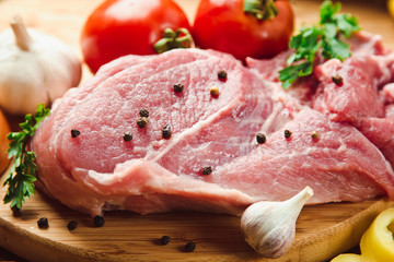 Raw meat on a wooden chopping board with fresh organic vegetables, onion, garlic, spices, peppercorn, salt, tomatoes and parsley for cooking. Kitchen ideas. Lunch, dinner