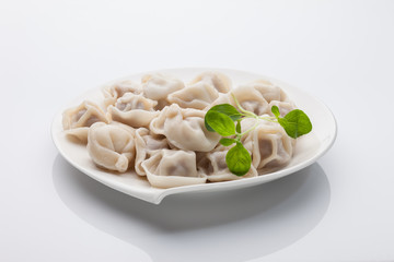 Pelmeni with oregano. On white plate and white background.