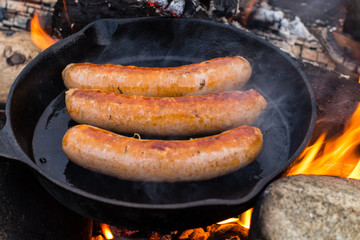 Cooking sausages in cast iron skillet on campfire while camping. Good and positive campfire food.