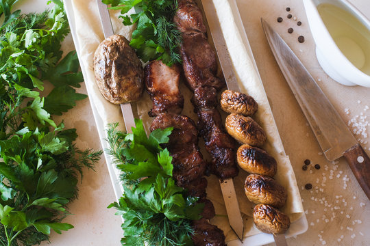 Shish-kebab with grilled vegetables on white dish. Meat, field mushrooms and fresh green herbs, barbecue and natural food preparing in restaurant
