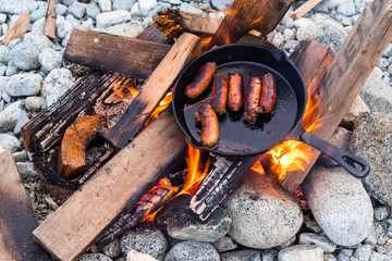 Cooking sausages in cast iron skillet on campfire while camping. Good and positive campfire food.