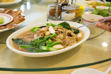 wide rice noodle, kale and mushroom with gravy soup on white dish and Thai seasoning in background