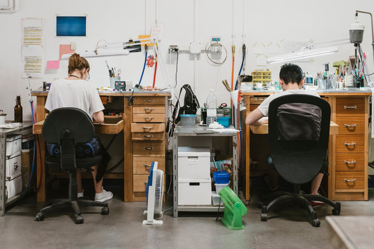 Rear view of male and female jewellers working at jewellery workbench