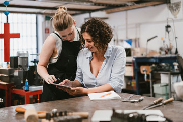 Two female jewellers looking at digital tablet at workbench