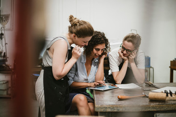Three female jewellers looking at digital tablet at workbench meeting