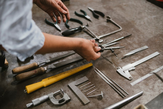 Hands of female jeweller laying out hand tools at workbench in jewellery workshop