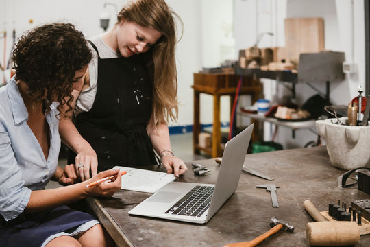 Two female jewellers drawing in notepad at workbench