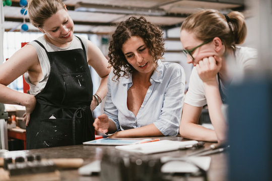 Three female jewellers looking at digital tablet at workbench meeting - Powered by Adobe