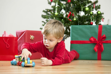 Happy Christmas Toddler with Gifts and Tree in his Modern Home with wooden floor and white walls: Playing with new Toys